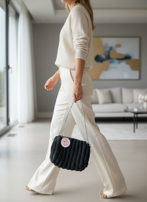 Woman in a white outfit holding a black handbag in a modern living room.