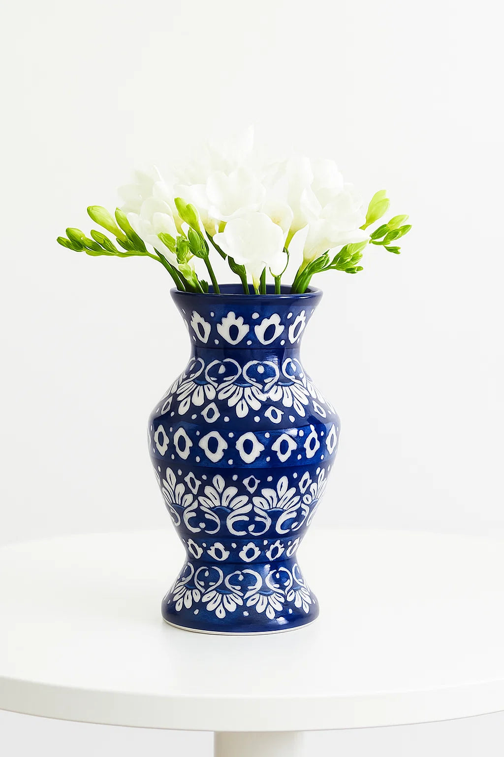 Blue and white patterned vase with white flowers on a white surface and background