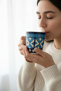 Woman drinking from a blue patterned mug against a white background
