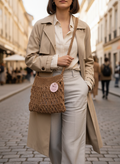 Woman in a beige trench coat with a brown textured handbag on a city street.