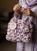 Person holding a purple and white crocheted handbag with a visible brand tag.